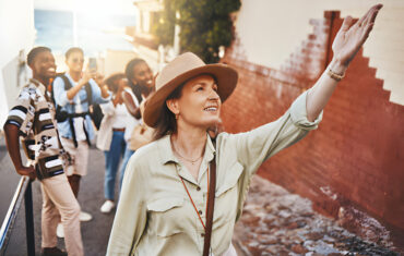 Image: A smiling tour guide standing in front of a historical monument, gesturing towards it. The guide holds a map, adding a touch of expertise to the travel experience. The backdrop features a blend of architectural marvels and natural beauty, promising a rich and immersive exploration. #ExpertGuide #CulturalExploration